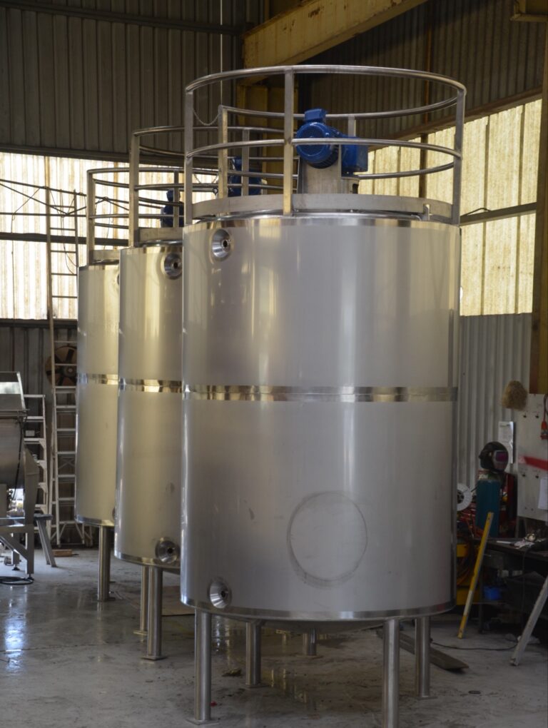 Three insulated 7,000 litre stainless steel milk ageing tanks with top-entry agitators and handrails